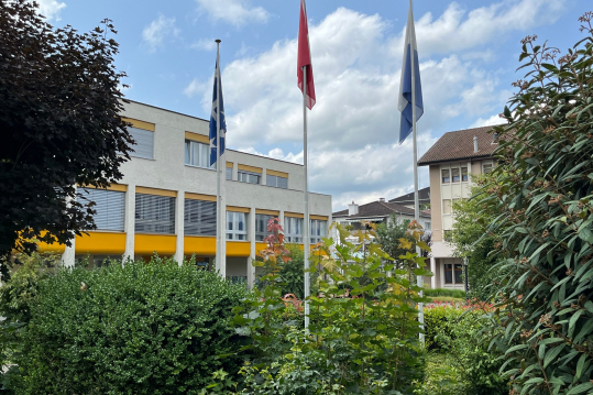 Drei Fahnen mit Gemeindehaus im Hintergrund